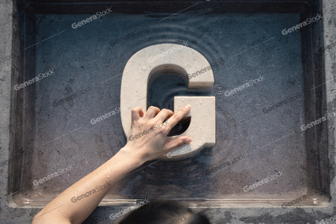 A person's hand touching a large carved stone letter G placed in