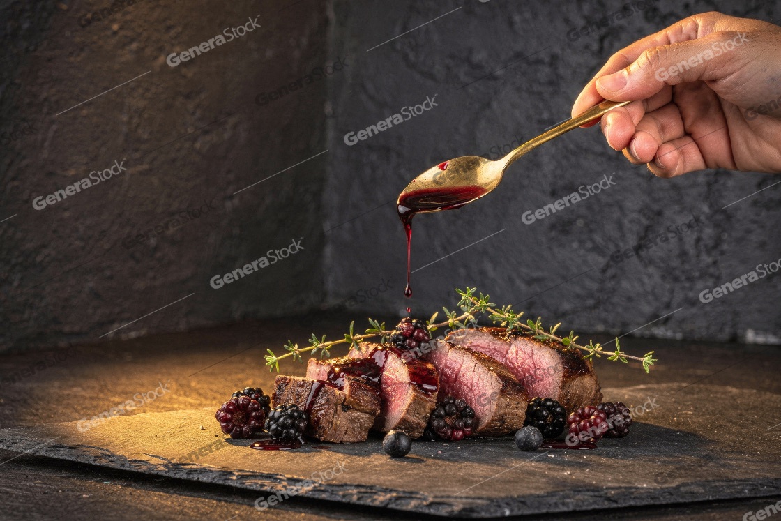 Chef pouring delicious blackberry sauce over juicy sliced duck b
