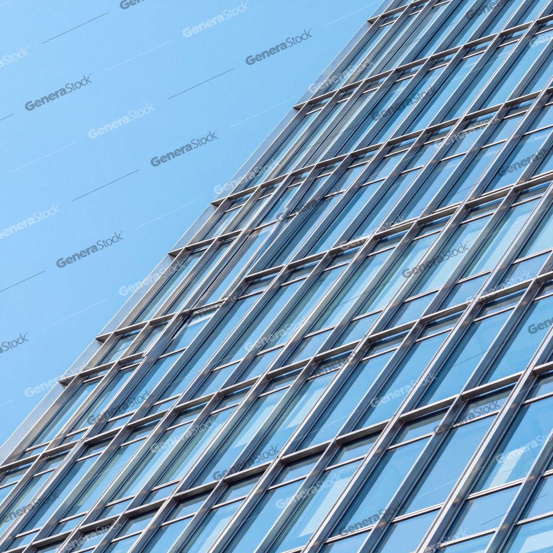 Modern glass skyscraper facade with a sleek architectural design featuring blue windows and a metallic frame set against a clear blue sky in a minimalist urban business district
