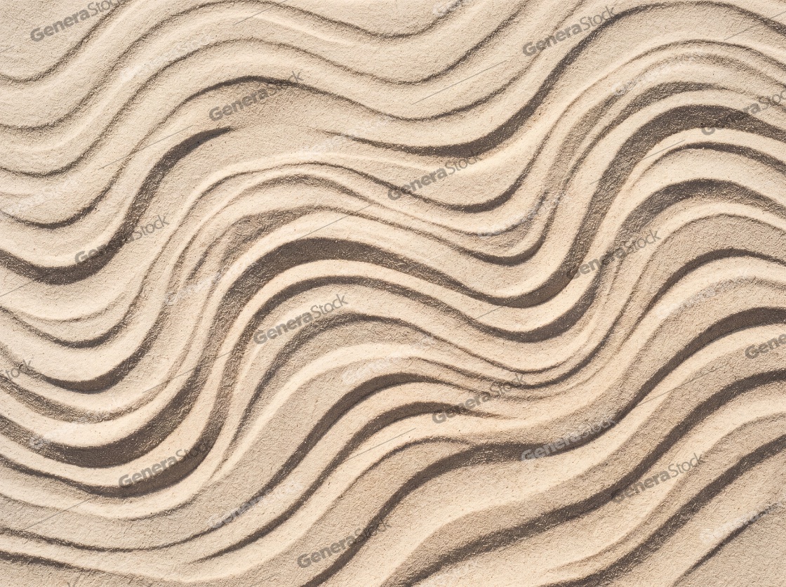 Top view of wavy patterns raked into light brown sand in a Zen garden, creating a peaceful abstract texture