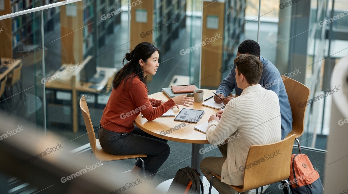 Group of multiethnic university students collaborating on a project at a round table in a contemporary library setting