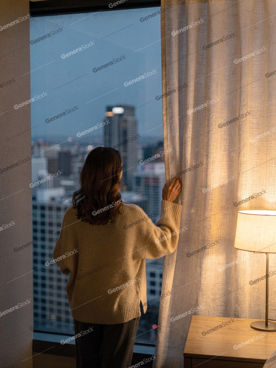 A woman in a cozy sweater opens the curtain to admire the city s