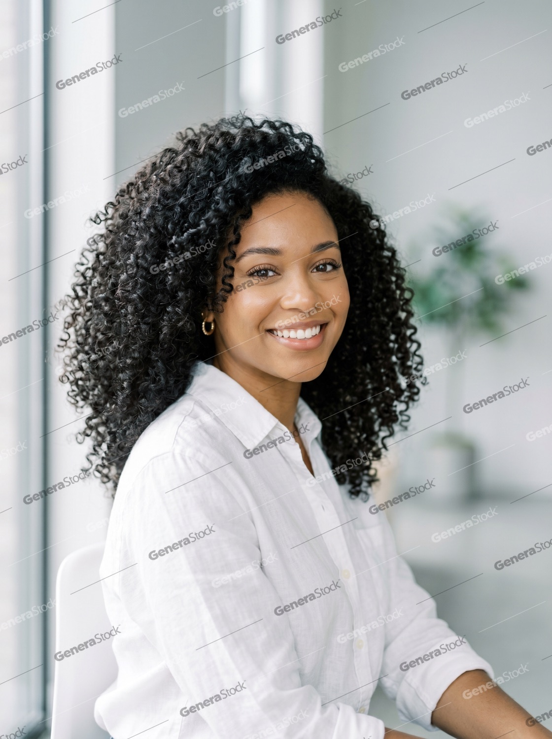 Portrait of a confident young Black woman with voluminous curly hair smiling in a bright modern office