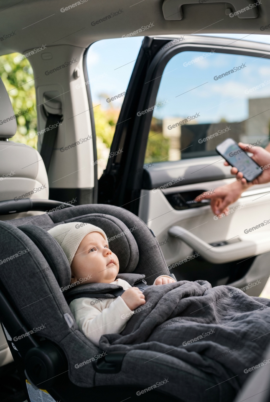 Adorable baby sitting in a secure car seat inside a modern vehicle while a parent uses a smartphone for navigation before a road trip