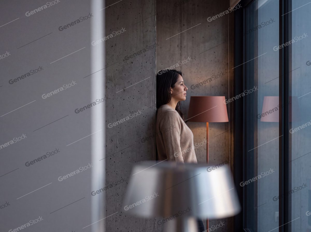 woman in a beige sweater against concrete, warm floor lamp, dusk