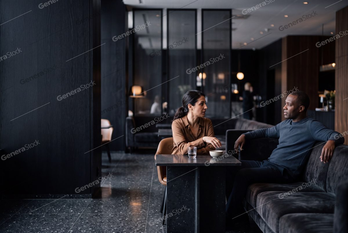 man and woman talking in a dark lounge, marble table, soft lamps