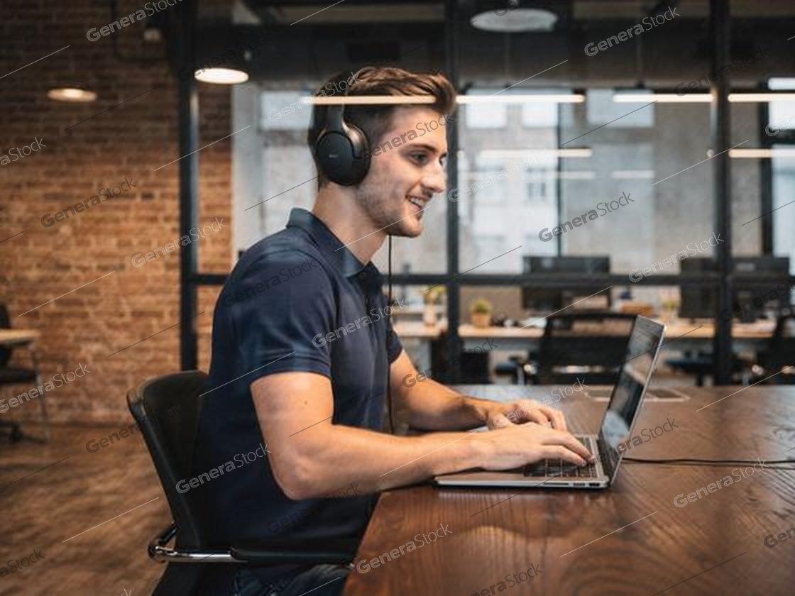 man with headphones typing on a laptop, exposed brick, glass wall
