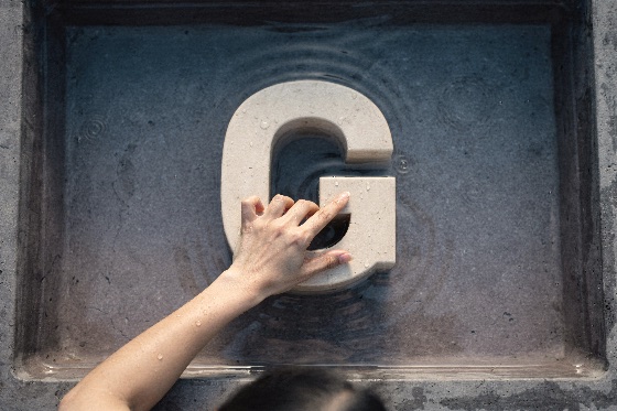 person, hand, touching, large, carved, stone, letter, placed, high-angle, shot, showing, resting, shallow, basin, filled, with, clear, water, fine, droplets, and, gentle, ripples, surround, the, sculpture, accentuating, tactile, calming, mood, scene, fountain, submerged, alphabet, typography, sculptured, concrete, surface, feeling, wet, minimalist, calm, serene, splash, symbol, character, initial, sign, font, textured, gray, liquid, finger, reach, top, view, high, angle, reflection, human, pure, sensory, tranquility, design, element, concept, pool, background, backgrounds, textures