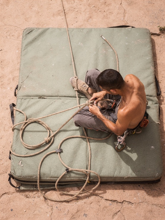 high, angle, view, shirtless, male, rock, climber, sitting, overhead, shot, green, bouldering, crash, pad, and, tying, knot, climbing, rope, the, athlete, preparing, his, safety, gear, before, embarking, outdoor, route, harness, preparation, top, man, equipment, outdoors, sports, adventure, extreme, sport, mat, security, active, lifestyle, athletic, ground, dirt, recreation, fitness, hobby, skill, concentration, focus, prep, adult, strength, training, dynamic, wilderness