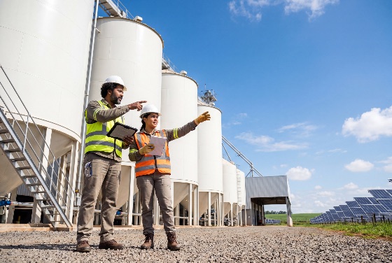 two, diverse, engineers, safety, gear, discussing, operations, renewable, energy, facility, with, silos, and, solar, panels, engineer, industry, silo, sustainability, green, teamwork, worker, vest, hard, hat, infrastructure, technology, environment, clean, professional, communication, planning, construction, power, industrial, outdoor, sky, storage, agriculture, logistics, management, technician, inspection, electricity, alternative, farm, field, woman, man, collaboration