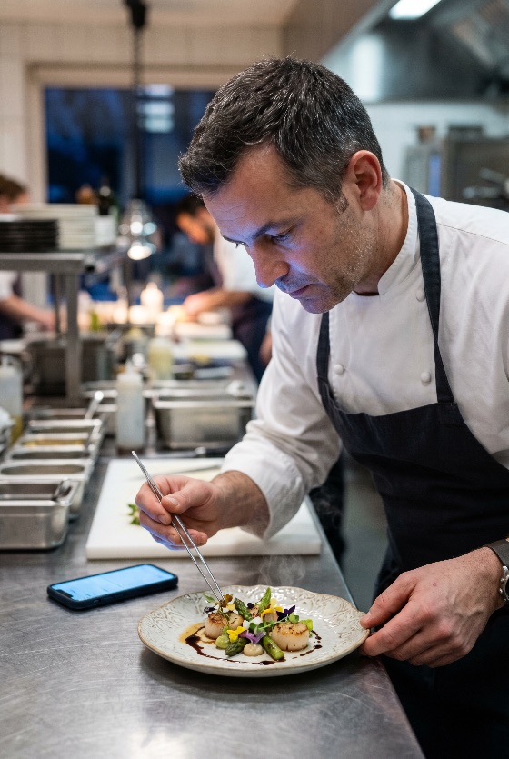 professional, male, chef, carefully, plating, gourmet, seafood, dish, with, seared, scallops, and, asparagus, high-end, commercial, kitchen, restaurant, cooking, food, culinary, fine, dining, precision, tweezers, man, uniform, apron, garnish, preparation, hospitality, gastronomy, work, meal, dinner, lunch, arts, styling, life, industry, staff, catering, luxury, delicious, healthy, fresh, drink