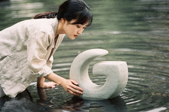 young, woman, beige, linen, jacket, gently, adjusting, curved, east, asian, wearing, light, shirt, leans, over, calm, dark, pool, water, touch, abstract, stone, sculpture, resting, the, shallows, gentle, circular, ripples, spread, across, surface, creating, peaceful, and, artistic, atmosphere, filled, with, mindfulness, nature, art, serene, pond, artist, craft, outdoor, reflection, harmony, zen, design, creative, lifestyle, ceramic, statue, tranquil, aesthetic, modern, profile, fine, elegance, contemplation, leisure, hand, concept, installation, pure, relaxed, shallow, side, view, smooth, natural, expression, arts, culture