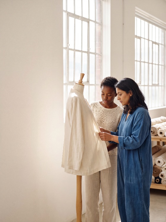 two, diverse, female, fashion, designers, working, together, bright, sunlit, studio, carefully, adjusting, cream-colored, linen, garment, mannequin, while, discussing, the, design, details, designer, dressmaker, tailor, clothing, creative, workshop, seamstress, women, multicultural, colleagues, teamwork, collaboration, professional, small, business, entrepreneur, airy, windows, natural, light, industrial, workspace, atelier, boutique, fabric, textile, rolls, cream, blue, sewing, craftsmanship, industry, sustainability, slow, handmade, startup, career, expertise, detail-oriented, african, american, south, asian, jumpsuit, sweater, stand, beauty