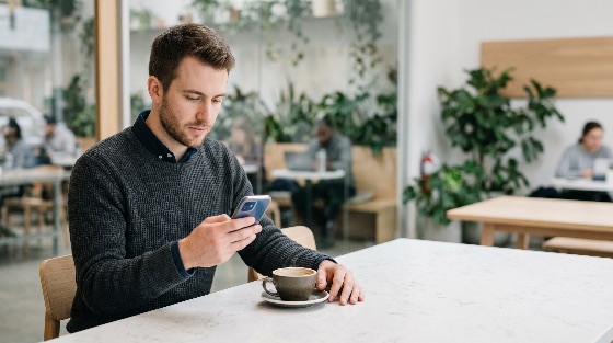 young, man, using, smartphone, while, sitting, table, with, cup, coffee, modern, cafe, mobile, phone, technology, lifestyle, male, internet, communication, shop, casual, person, adult, social, media, connection, digital, business, work, remote, freelance, indoor, drink, beverage, leisure, people, background, blurred, plants, green, urban, city, handsome, attractive, portrait, browsing, texting, messaging, online, app, wireless, electronic, gadget, device