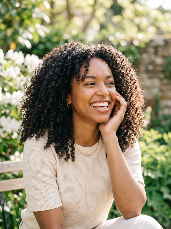 portrait, happy, young, black, woman, with, curly, hair, laughing, sunny, garden, outdoors, smile, joyful, african, american, natural, summer, lifestyle, beautiful, person, female, nature, park, leisure, wellness, positive, cheerful, ethnic, mixed, race, beauty, casual, sunshine, spring, greenery, teeth, hand, face, people