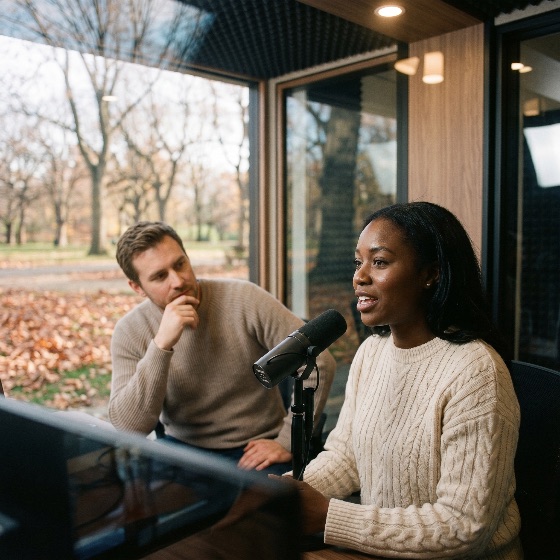 young, african, american, woman, recording, podcast, with, colleague, modern, studio, microphone, broadcast, radio, interview, man, diverse, colleagues, professional, audio, media, communication, speech, listening, autumn, park, window, office, technology, content, creator, influencer, storytelling, collaboration, creative, lifestyle, talk, show, streaming, digital, narrator, voiceover, announcer, hosting, podcasting, sound, equipment, indoor, daytime, casual, sweater, knitwear, people, adult, business, startup