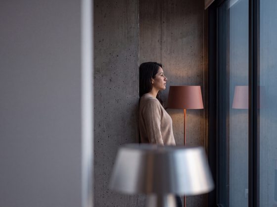 woman in a beige sweater against concrete, warm floor lamp, dusk