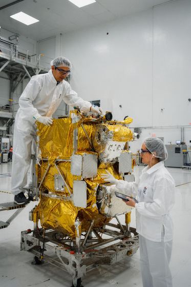 two engineers working on a gold foil satellite, white cleanroom