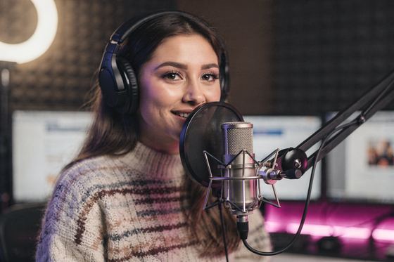 woman with headphones smiling at a studio mic, ring light, pink glow