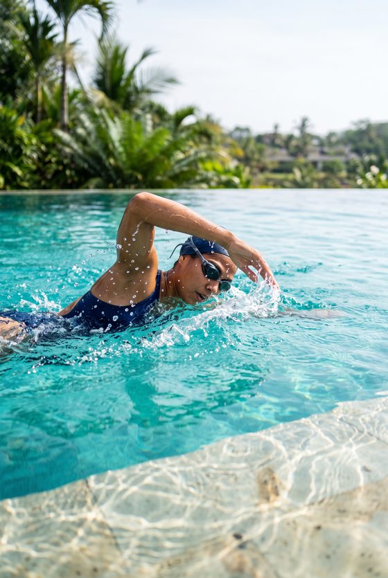 swimmer doing front crawl, turquoise water, tropical garden behind