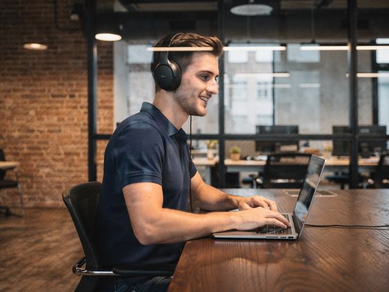 man with headphones typing on a laptop, exposed brick, glass wall