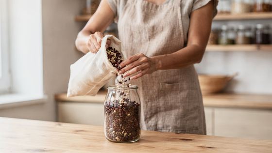 woman in linen apron filling a jar from a cloth bag, pantry shelves