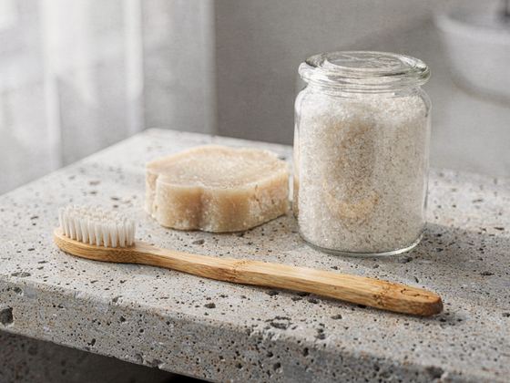 solid soap bar, jar of bath salt and a bamboo brush on stone
